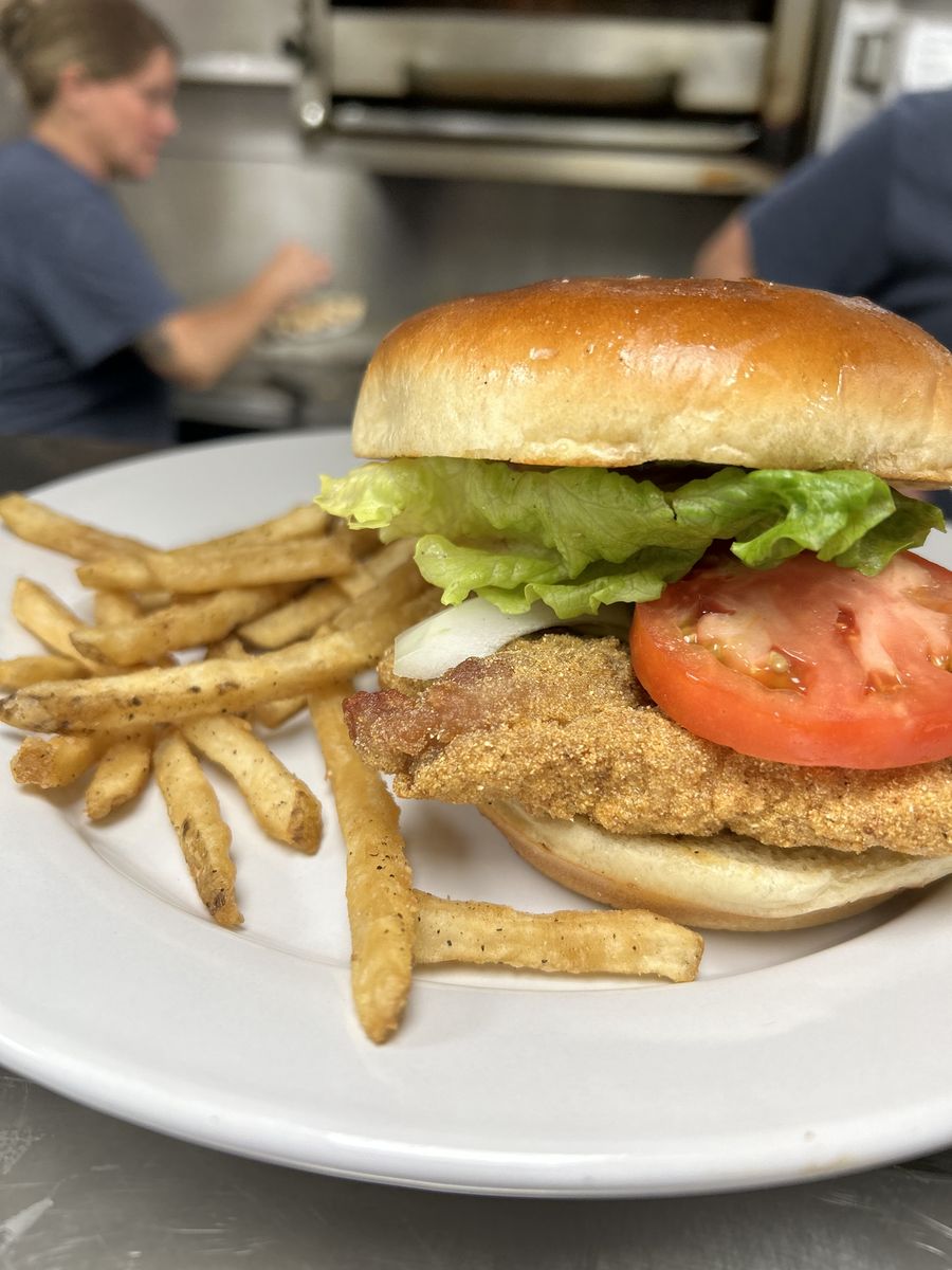 A golden fried catfish sandwich with lettuce and tomato, served with fries