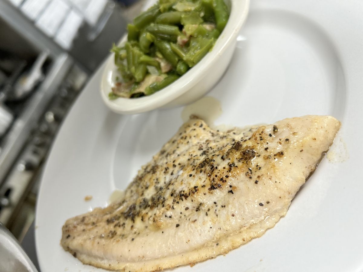 A seasoned fish fillet plated with a side of homestyle green beans