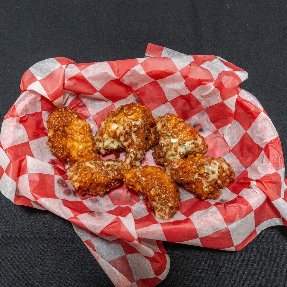 Six golden fried chicken wings topped with melted cheese, served in a red-and-white checkered basket liner.