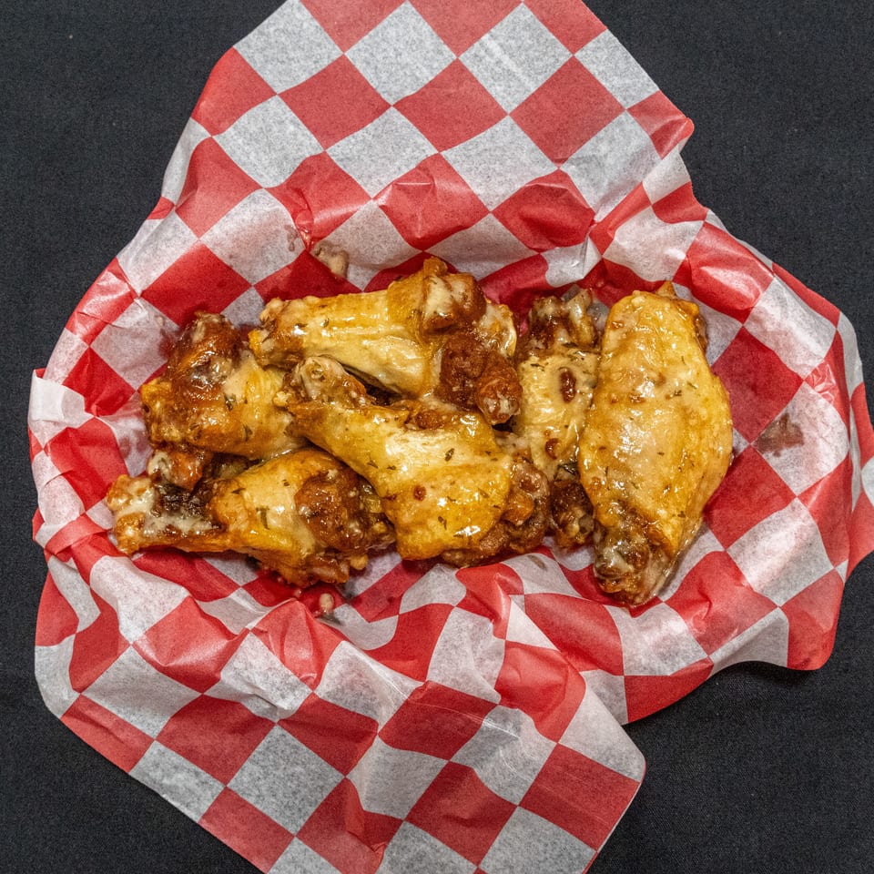 Golden-brown chicken wings served on red-and-white checkered paper over a dark surface.