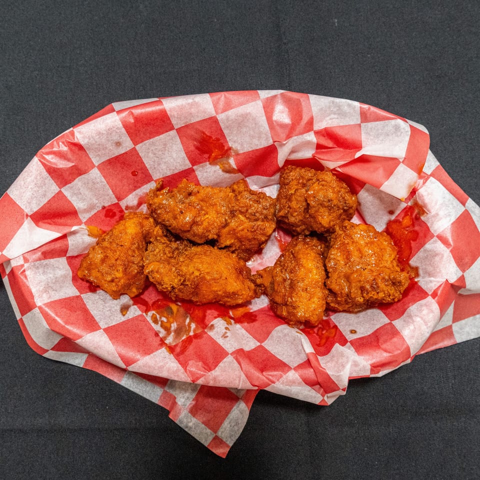Basket of crispy fried chicken pieces served on red-and-white checkered paper.