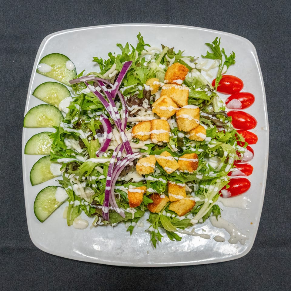Garden salad topped with crispy golden croutons, shredded purple cabbage, cucumber slices, cherry tomatoes, and creamy dressing.
