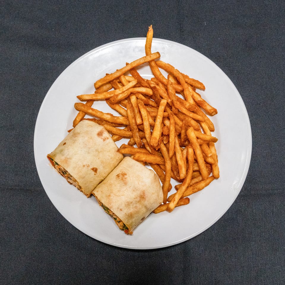 Two toasted wrap halves served with a generous portion of golden seasoned fries on a white plate.