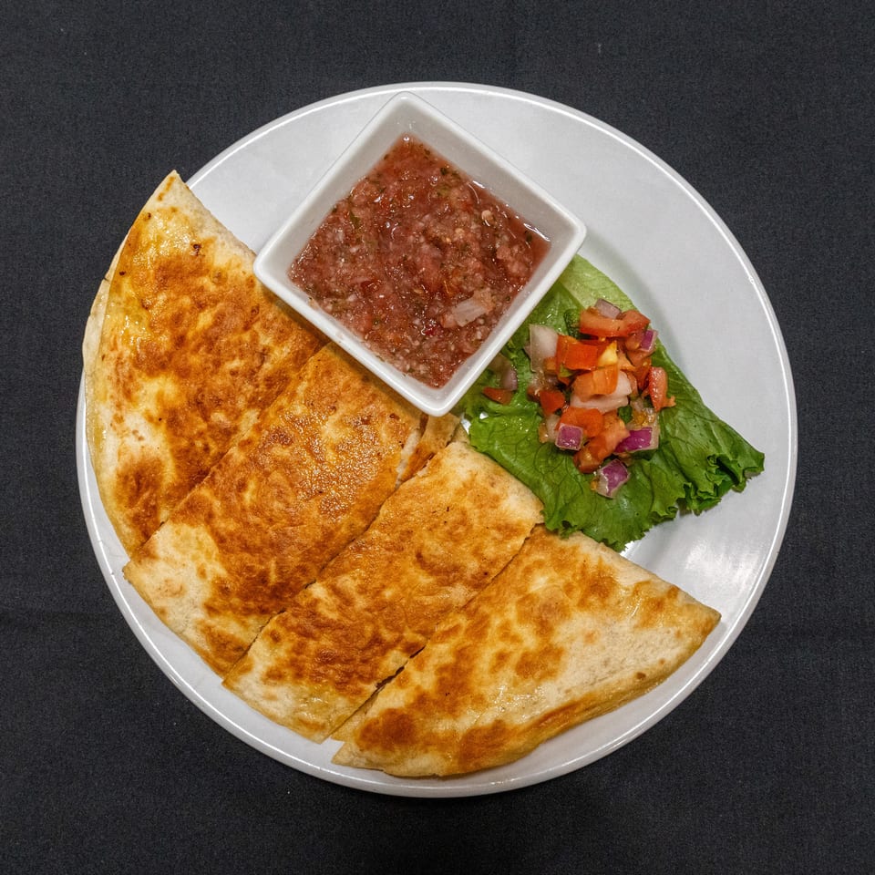 Golden-brown quesadilla wedges served with fresh salsa and a lettuce salad on a white plate.